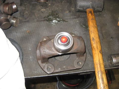 1994 Ford Bronco - A driveshaft yoke with a red zerk fitting is shown on a workbench next to a rubber mallet and other parts.
