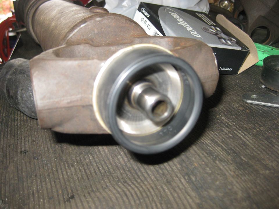 Driveshaft part with a seal and metal shaft, resting on a wooden surface. A box with text is in the background