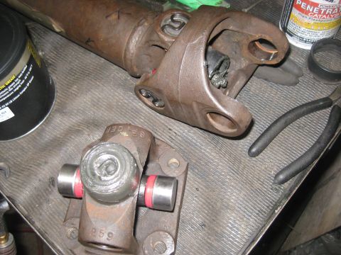 1994 Ford Bronco - Close-up of driveshaft parts, including a universal joint, with tools and lubricant on a textured surface.