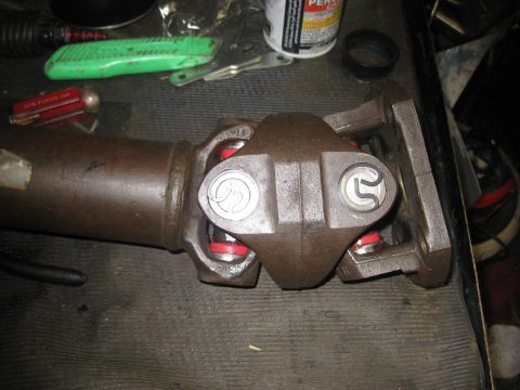 1994 Ford Bronco - Close-up of a driveshaft U-joint assembly, showing red seals and silver caps, resting on a workbench.