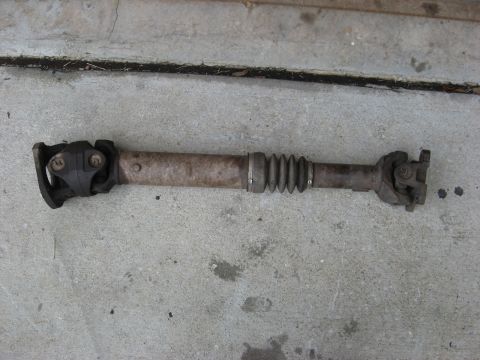 1994 Ford Bronco - A driveshaft lies on a concrete surface, showing its universal joints and protective rubber boot.