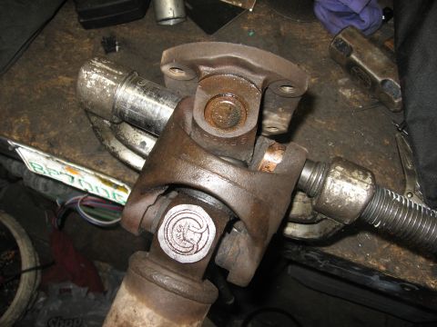 1994 Ford Bronco - A driveshaft U-joint is shown in detail, a circular emblem on one of its yokes.