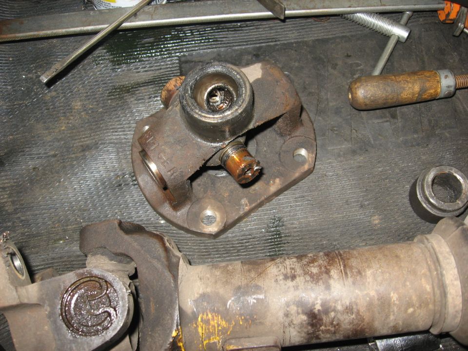 Driveshaft universal joint with grease and wear, next to a driveshaft section. Tools are visible in the background