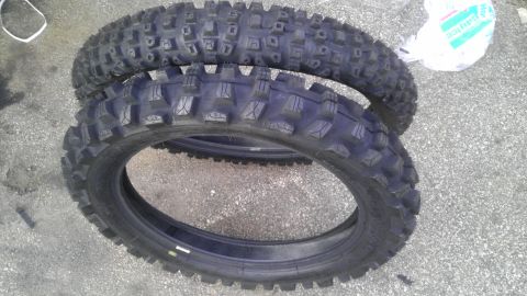 1989 Ford Bronco - Two knobby dirt bike tires are shown stacked on a paved surface.