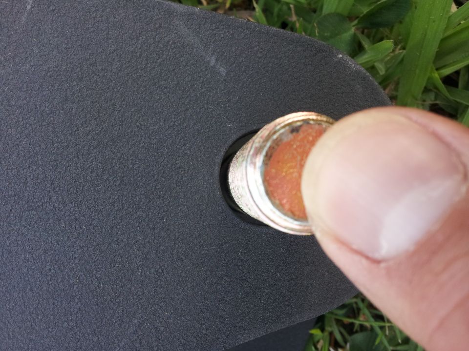 Close-up of a finger pushing a round, orange-colored part into a textured black surface