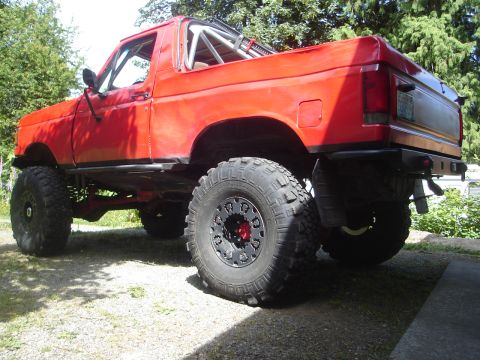 1989 Ford Bronco - Modified 1989 Ford Bronco with off-road tires and a roll cage, seen from the rear quarter angle.