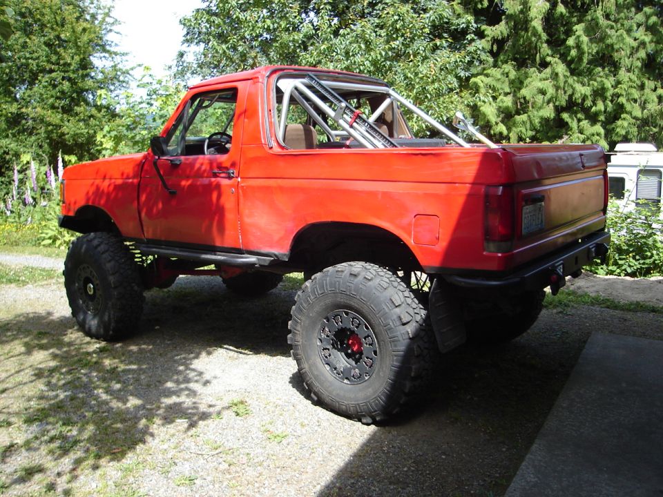 Red lifted Ford Bronco with roll cage, parked outside
