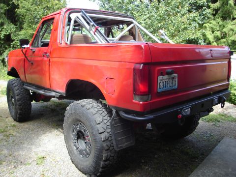 1989 Ford Bronco - This lifted 1989 Ford Bronco features off-road tires, a custom bumper, and a roll cage visible through the open top.