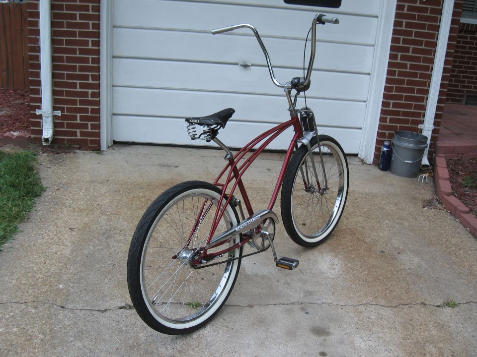 Red cruiser bicycle with chrome handlebars and whitewall tires parked in front of a garage