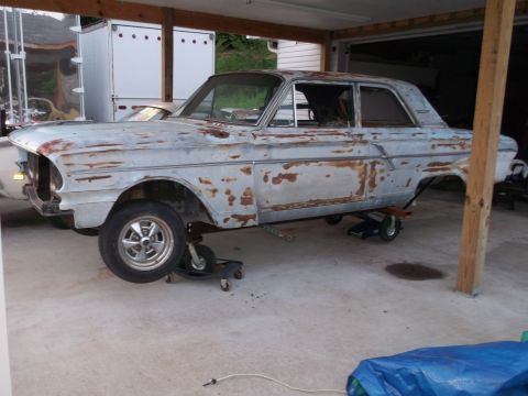 1971 Ford Ranchero - A heavily rusted light blue sedan sits on dollies under a carport, awaiting restoration.