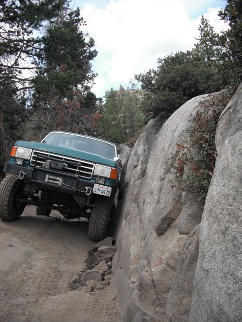 1991 Ford Bronco - 1991 Ford Bronco tackling a challenging off-road obstacle on a dirt and rock path.