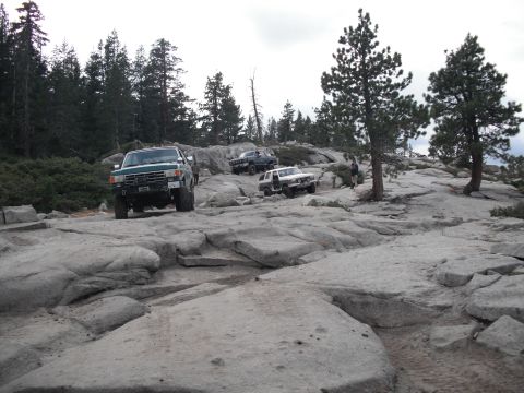 1991 Ford Bronco - Several off-road vehicles navigate a challenging rocky landscape under a cloudy sky.