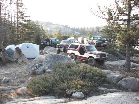 1991 Ford Bronco - A group of off-road vehicles and tents are set up in a rocky, wooded area, with a 1991 Ford Bronco prominently featured.