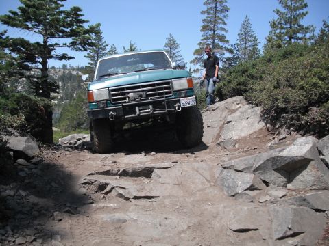 1991 Ford Bronco - A 1991 Ford Bronco navigates a rocky off-road path under a clear blue sky.
