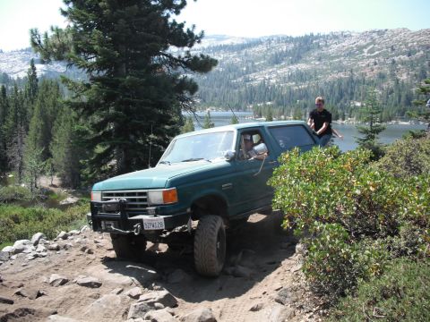 1991 Ford Bronco - A green 1991 Ford Bronco navigates a , rocky path near a lake.
