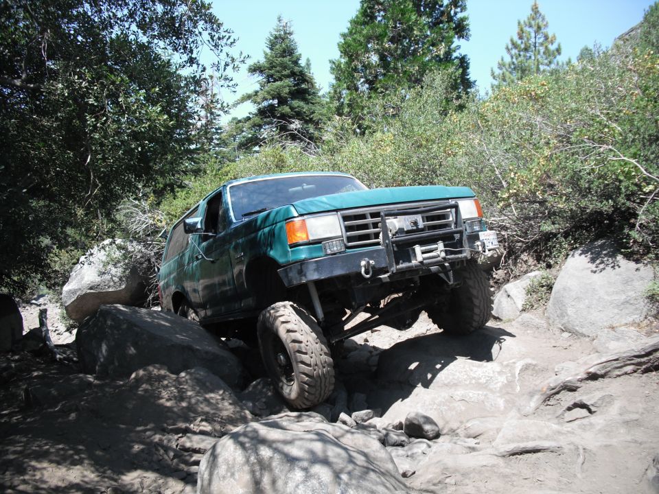 1991 Ford Bronco navigating a boulder-strewn trail with trees and sky in background