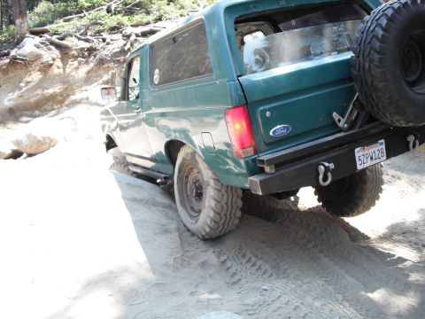 1991 Ford Bronco - A green 1991 Ford Bronco navigates a sandy, off-road trail with a spare tire mounted on the rear.