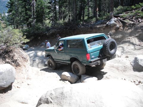 1991 Ford Bronco - This 1991 Ford Bronco is shown tackling a challenging, rocky trail with trees and boulders surrounding it.