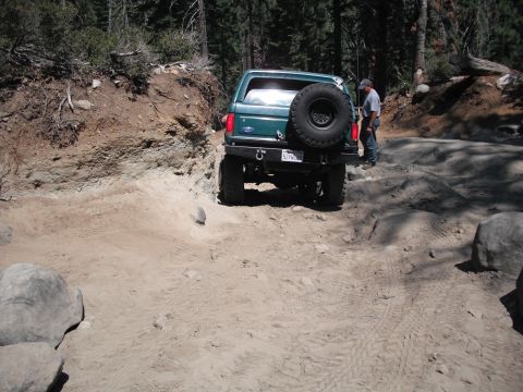 1991 Ford Bronco - Green 1991 Ford Bronco navigating a challenging off-road path in a wooded area.