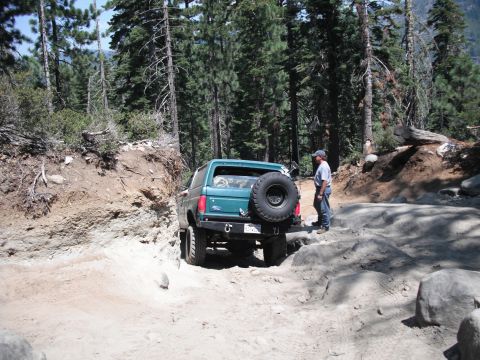 1991 Ford Bronco - A 1991 Ford Bronco tackles a challenging off-road path in a wooded area.