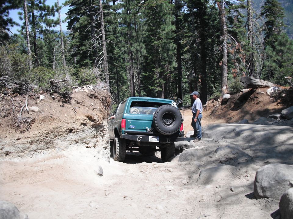Green 1991 Ford Bronco navigating a rocky, dirt trail with a person standing nearby