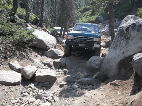 1991 Ford Bronco - A green SUV navigates a challenging rocky trail, with another vehicle following behind.