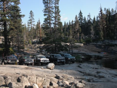 1991 Ford Bronco - Several off-road vehicles are parked on a rocky landscape near a wooded area.