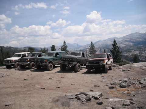 1991 Ford Bronco - A group of four-wheel drive SUVs are parked on a rocky, mountainous landscape under a partly cloudy sky.