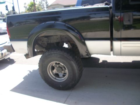 2001 Ford F-250 - Side view of a black and silver pickup truck, likely a 2001 Ford F-250, with visible fender flares and a large tire.