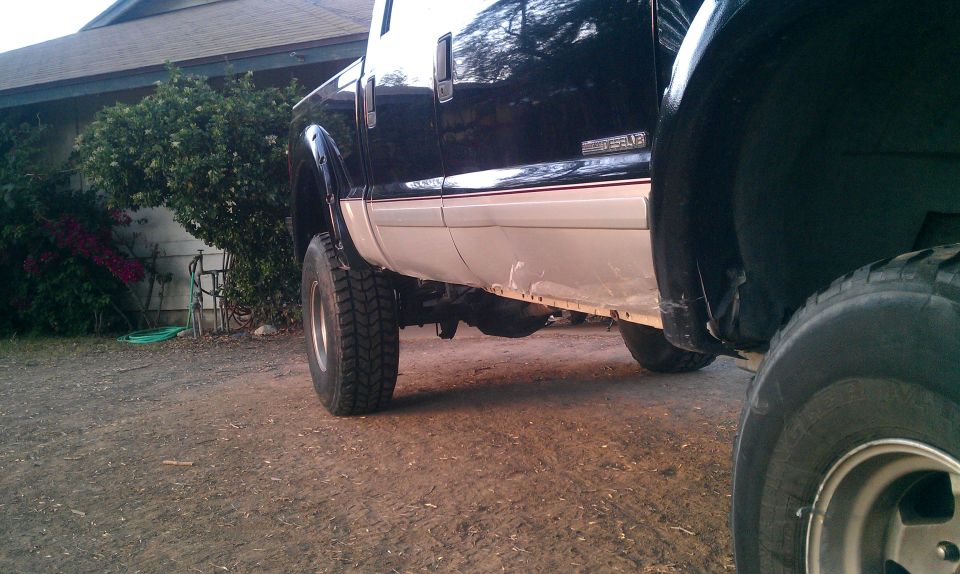 Side view of a black and tan 2001 Ford F-250 truck, parked outdoors. Another vehicle's tire is in the foreground