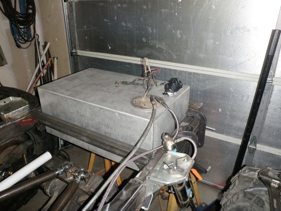 Aftermarket aluminum fuel tank with sender unit and fuel lines connected, mounted on a workbench