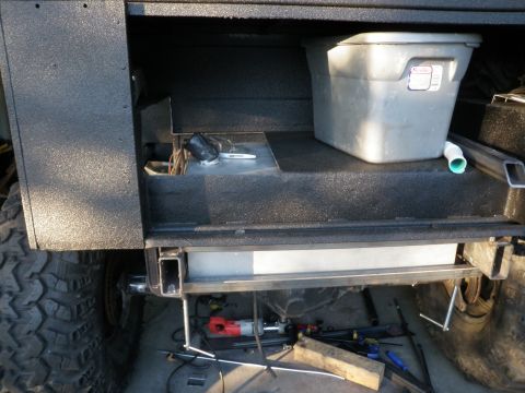 1961 International Scout 800 - The rear chassis of a vehicle shows a large storage bin and fuel tank, with tools and wiring exposed below.