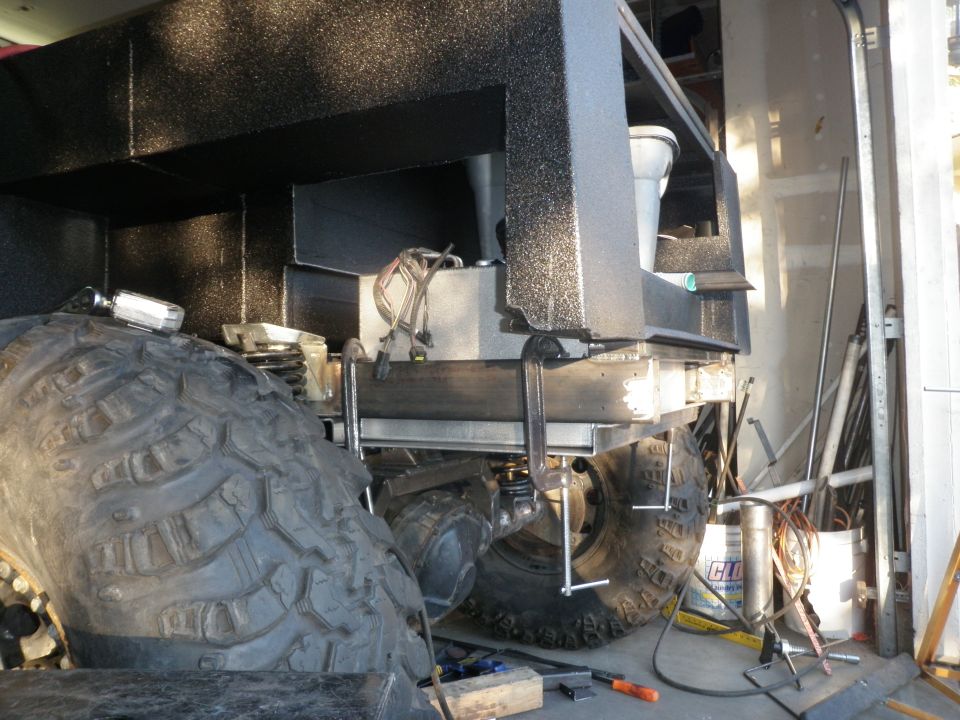Rear chassis and large tire of a vehicle under construction, showing fuel tank and suspension components