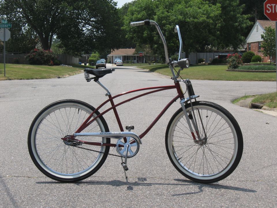 Maroon cruiser bicycle with chrome handlebars and white-wall tires parked on asphalt