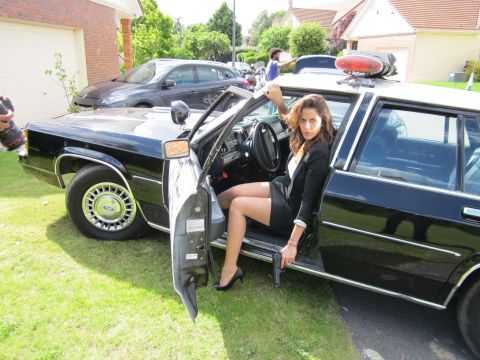 1991 Ford LTD Crown Victoria - A woman sits in the driver's seat of a black police car, holding a handgun.