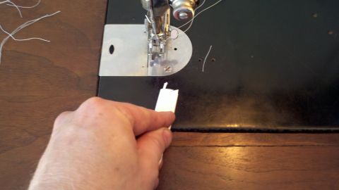 1900 Ford C-350 (Centurion Conversions) - Close-up of a hand feeding fabric into a sewing machine, with the Supermotors.net logo in the corner.