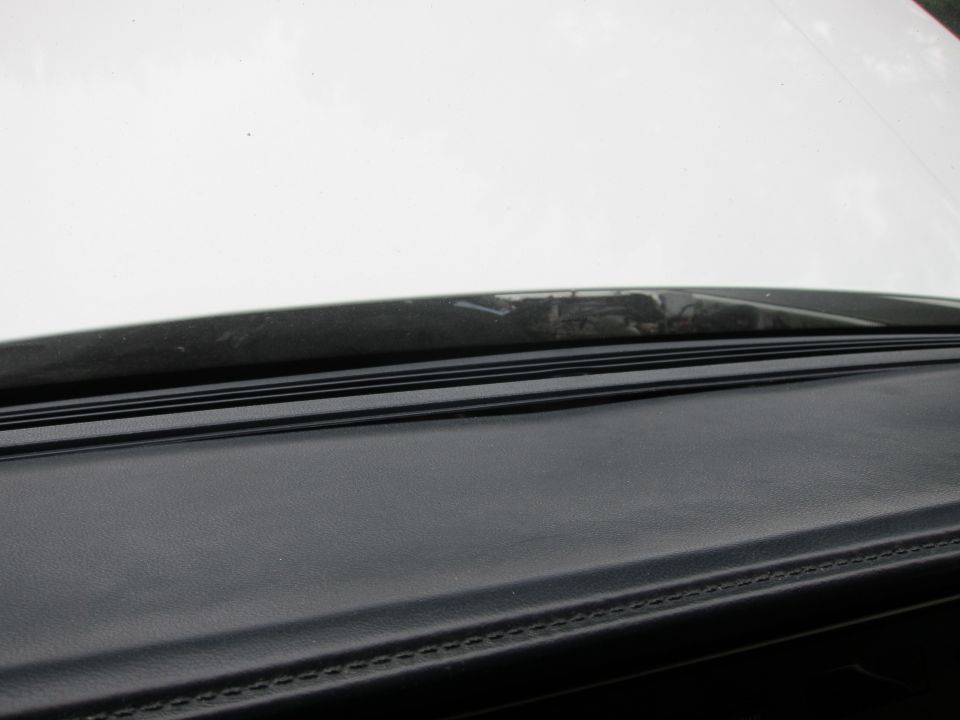 Car dashboard and part of the windshield. The dashboard is black with visible stitching