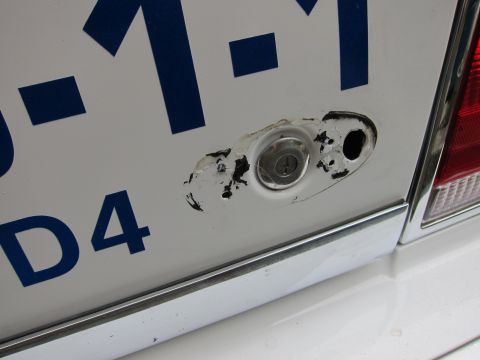 1991 Ford LTD Crown Victoria - The rear of a white vehicle displays blue lettering and a damaged lock mechanism near the trunk.
