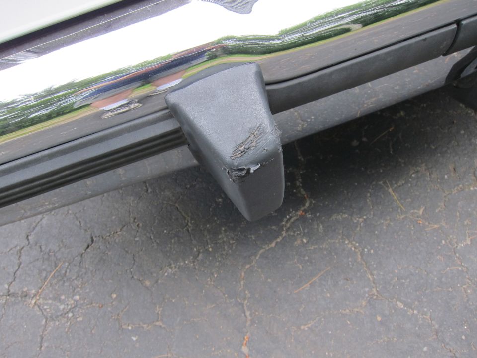 Gray plastic bumper corner with scuffs and chipped paint, attached to a chrome trim piece on a vehicle