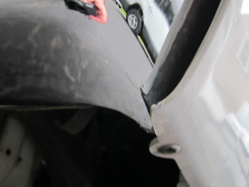 Close-up of a car's fender and wheel well, with another white vehicle visible in the background