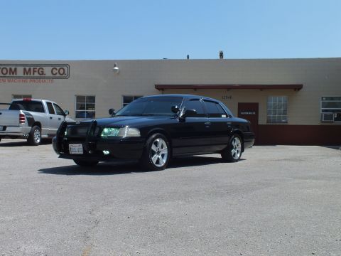 2003 Ford Crown Victoria - black full-size Ford sedan with brush guard and chrome wheels sits before a manufacturing building