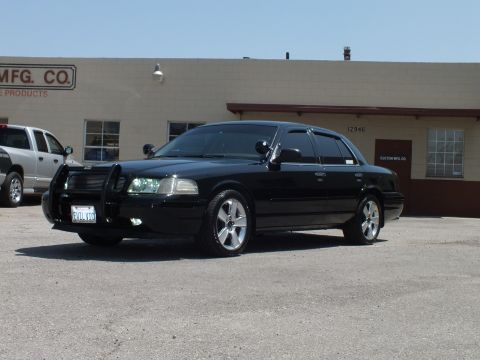 2003 Ford Crown Victoria - Front-quarter view of a lowered black Crown Victoria parked by an industrial building, push bar fitted