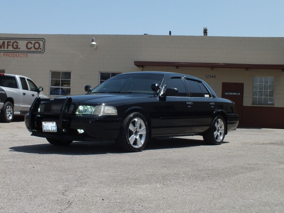 Black Ford Crown Victoria sedan with chrome push bar, dark wheels and tinted windows, California plate