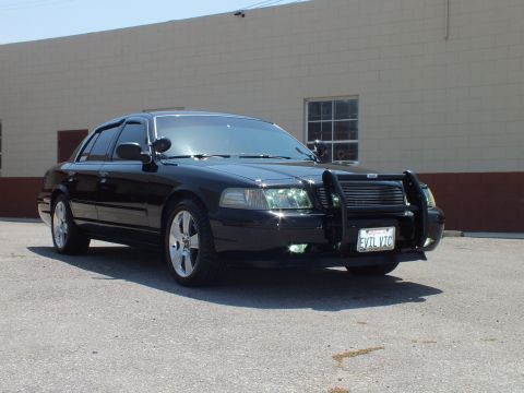 2003 Ford Crown Victoria - Glossy black sedan from front-right, push bar and chrome wheels against masonry wall