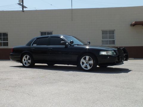 2003 Ford Crown Victoria - Side profile of lowered black sedan, push bar visible at front, industrial backdrop