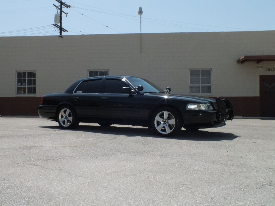 Passenger-side view of black full-size sedan with chrome wheels parked near tan building
