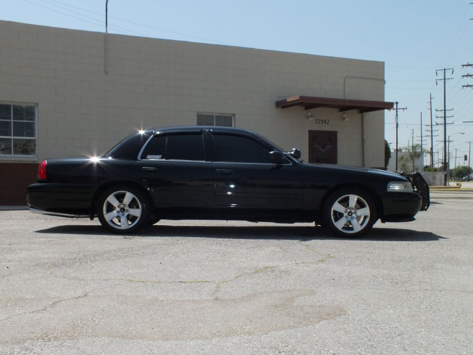 Black full-size sedan driver-side profile, chrome wheels, tinted windows, industrial lot