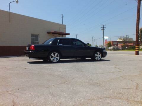 2003 Ford Crown Victoria - Black sedan rear-left angle, taillights and trunk visible, building and stop sign behind