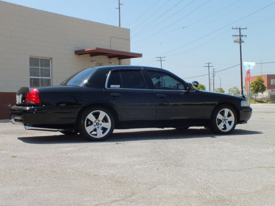 Black full-size sedan rear-quarter from passenger side with chrome wheels on industrial lot