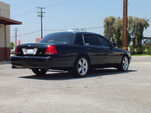 2003 Ford Crown Victoria - Rear-right view of black Crown Victoria on cracked lot, Ford badge and taillights